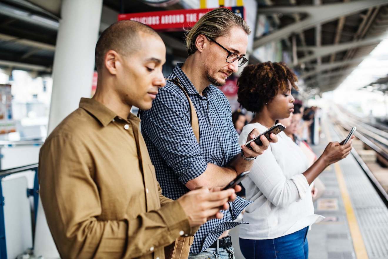 two men and a woman staring at phones while waiting on a train platform