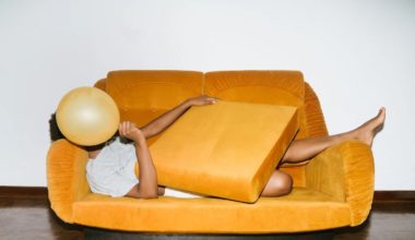 man lying on orange couch covering face with balloon