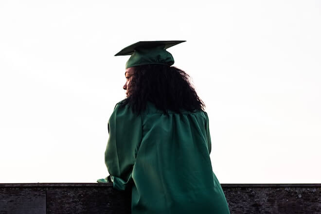 A woman stands over a balcony with a graduation cap and gown on