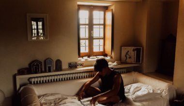 Man slouching over his legs while sitting on bed in a dark room