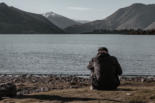 A man sits by a mountainous beach
