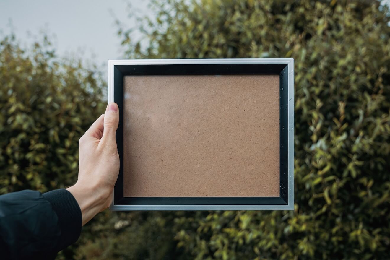 A woman holds a blank picture frame in front of trees