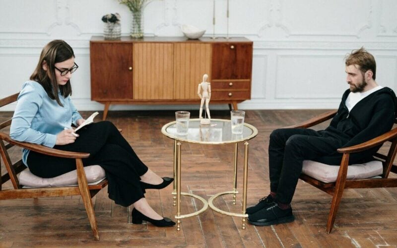 disheveled man speaking to a woman with a notepad